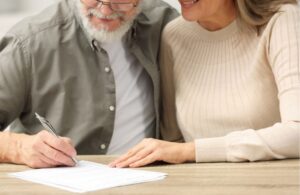 senior man and woman sitting at table signing a form