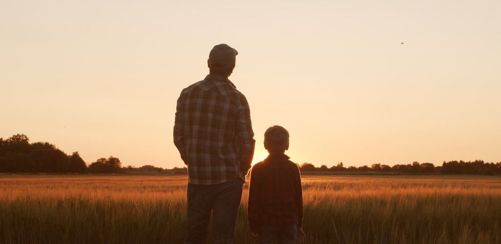 father and son standing in field at sunset