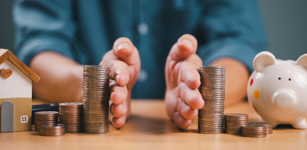 hands splitting money and a piggy bank and money with a model house apart