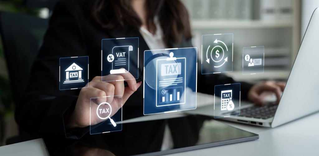 woman working on tablet and laptop with illustrated tax and other business icons