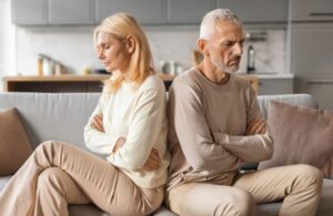 wealthy older couple sitting on couch back-to-back upset