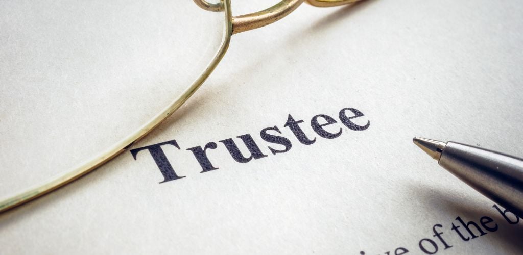 trustee typed on paper with pen and glasses also sitting on paper