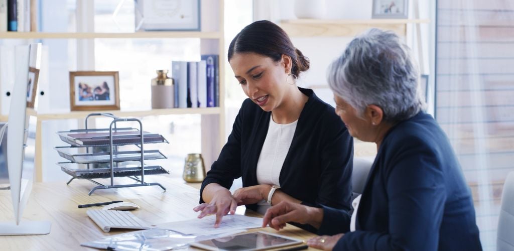 two women at a desk talking and reviewing documents